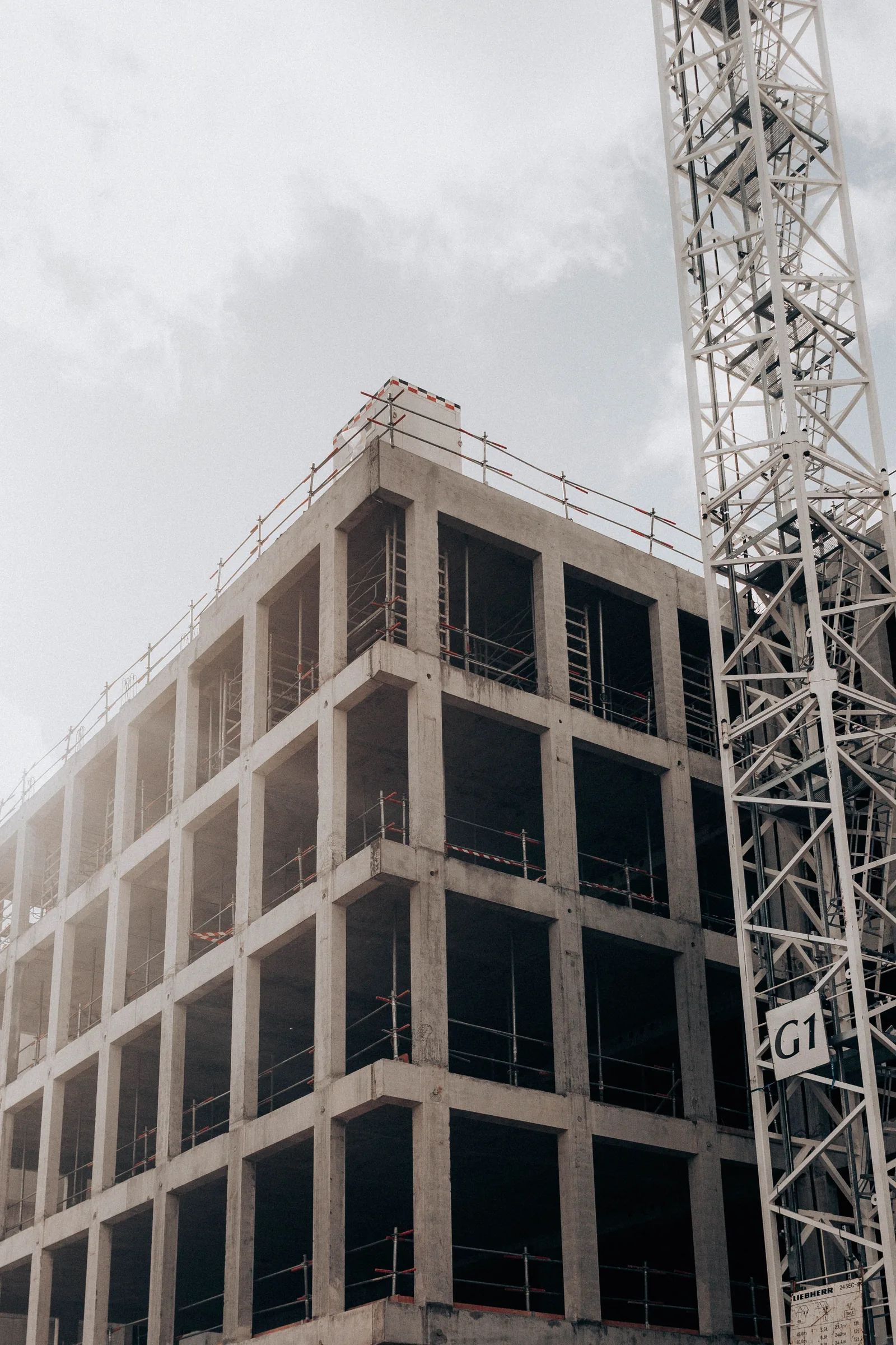 A concrete frame of a new building under construction, with scaffolding and a crane