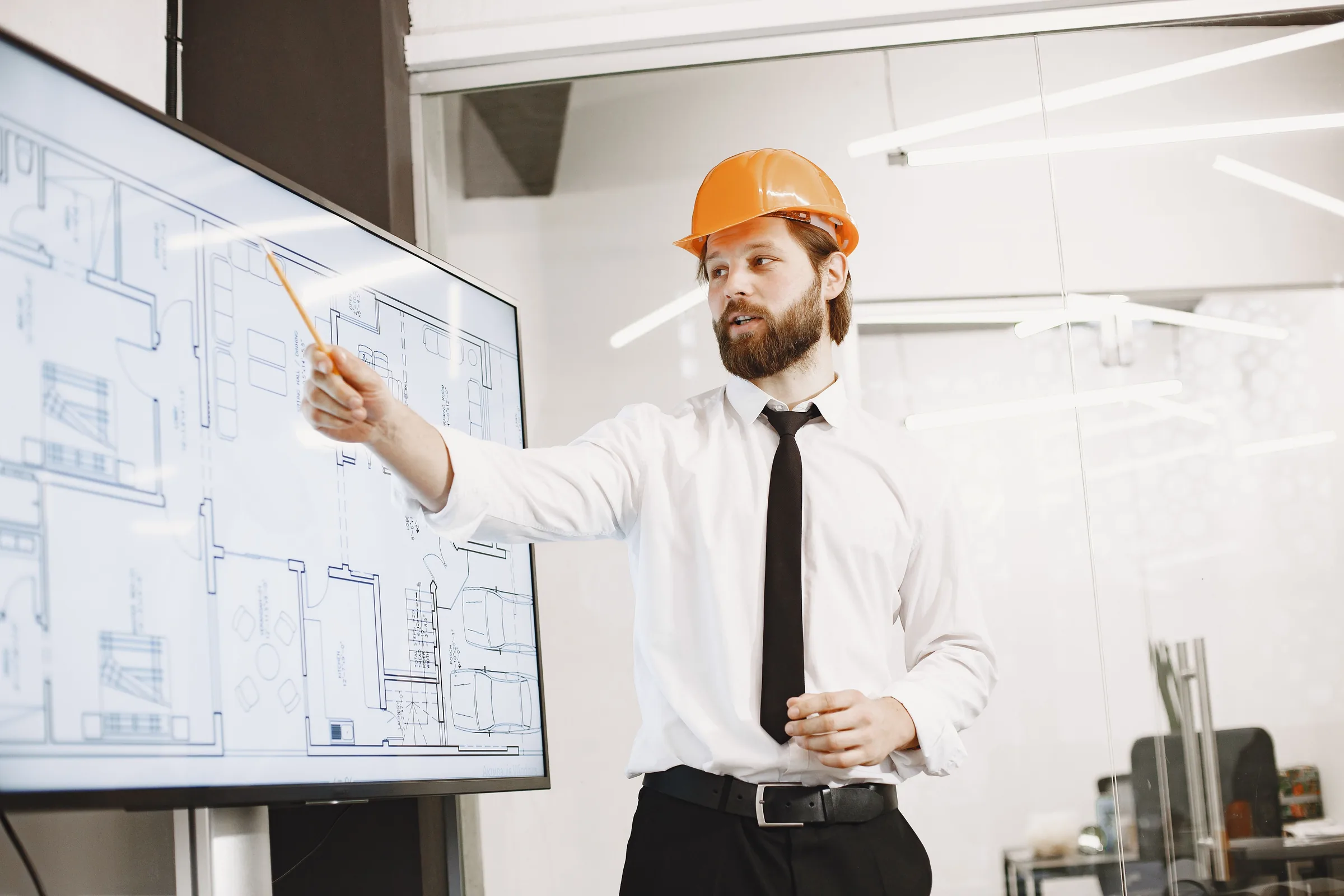 An engineer in a hard hat presenting a building plan on a large screen