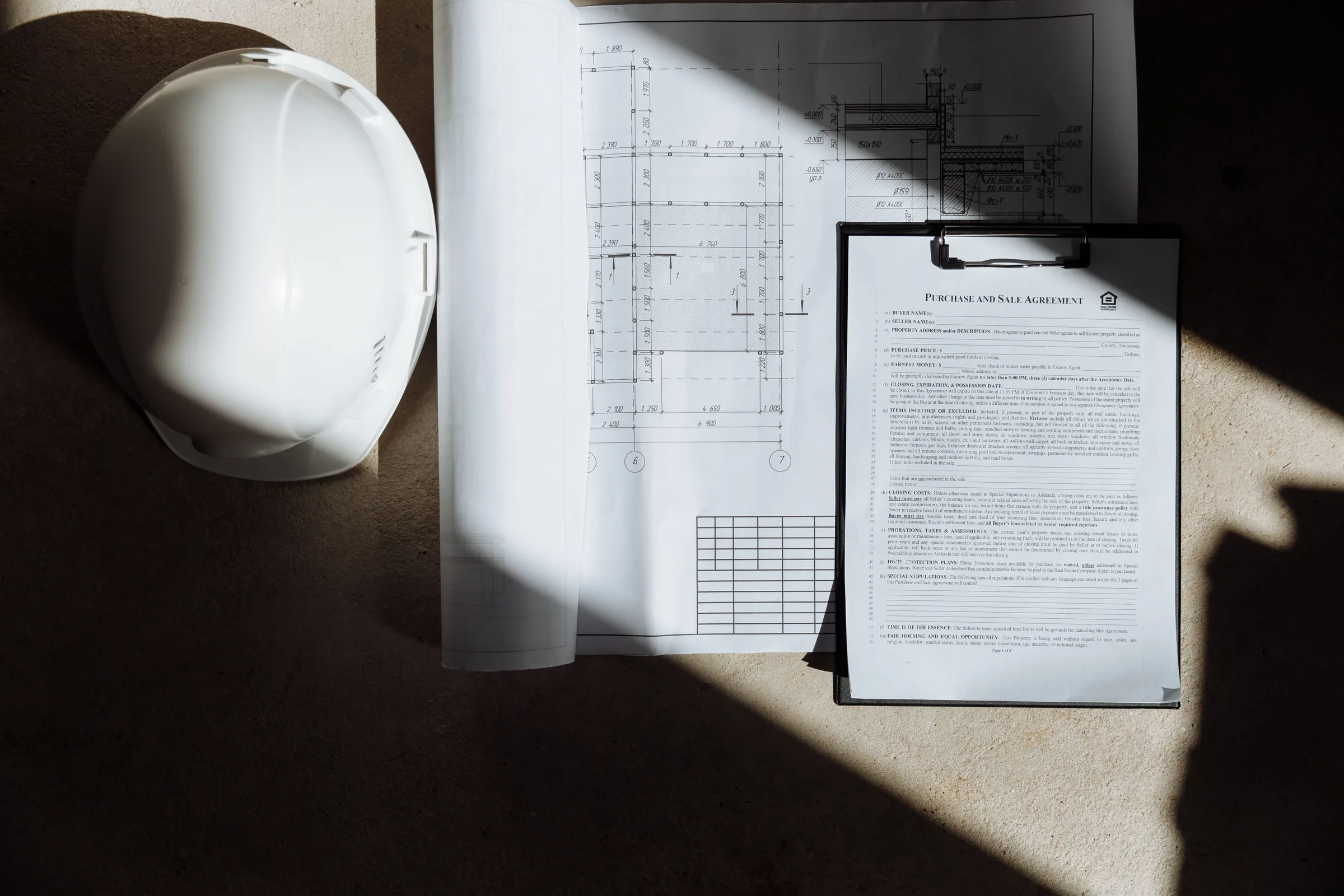 A white hard hat resting on architectural drawings in strong sunlight