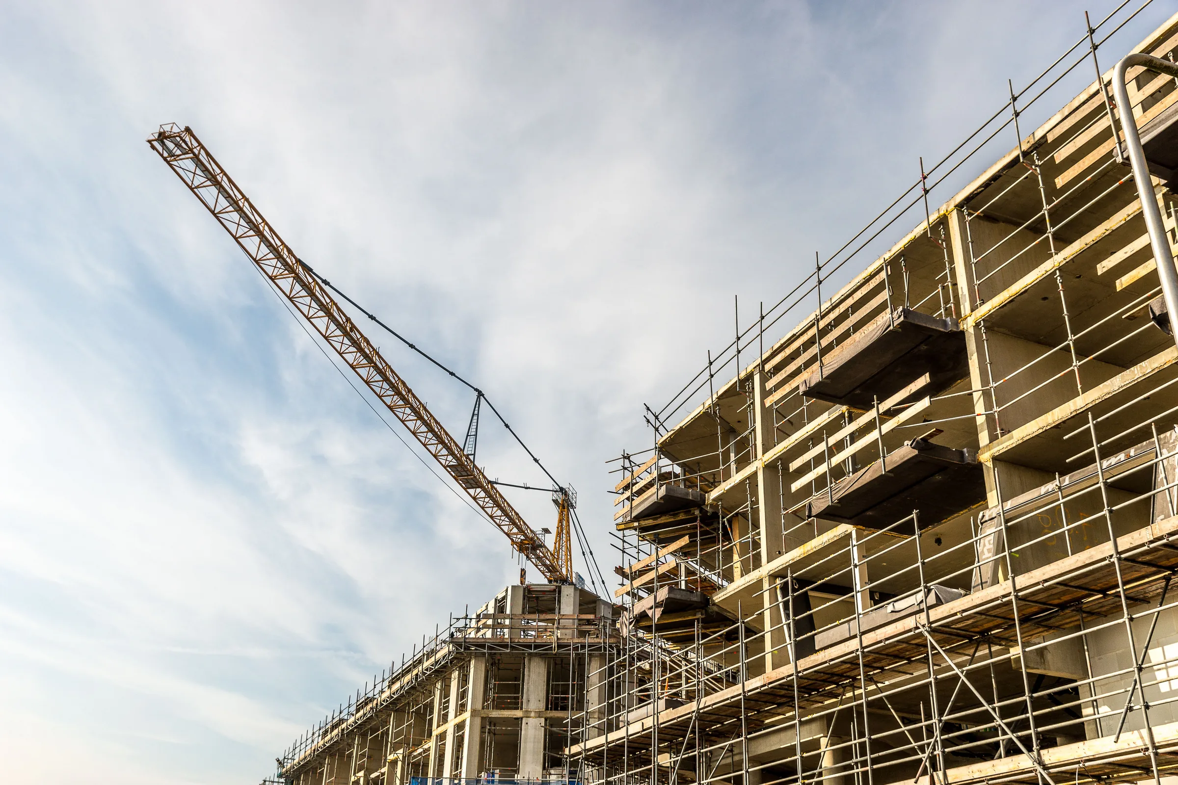 A tower crane over a scaffolded building under construction against the sky