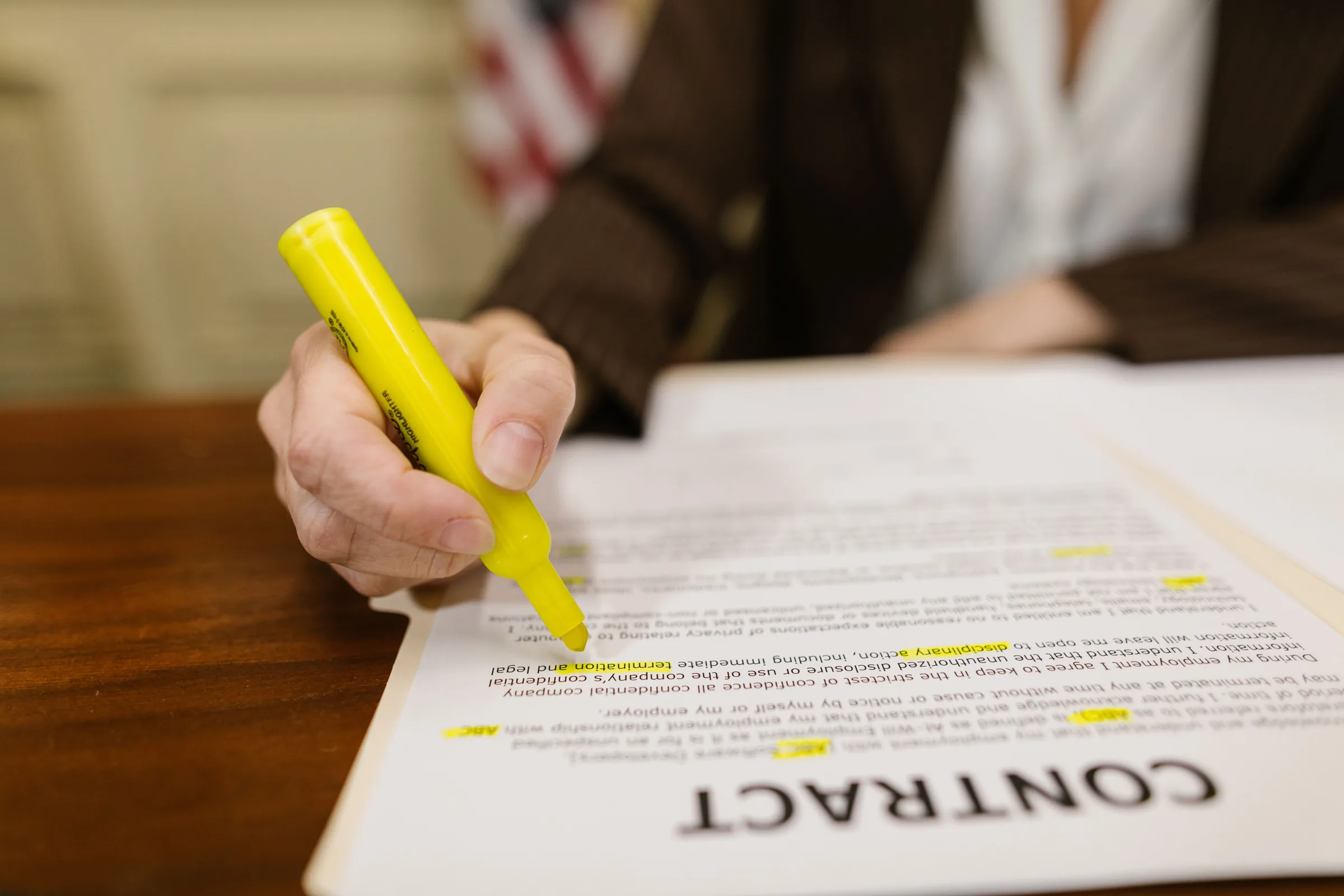 A hand marking clauses on a printed contract with a highlighter