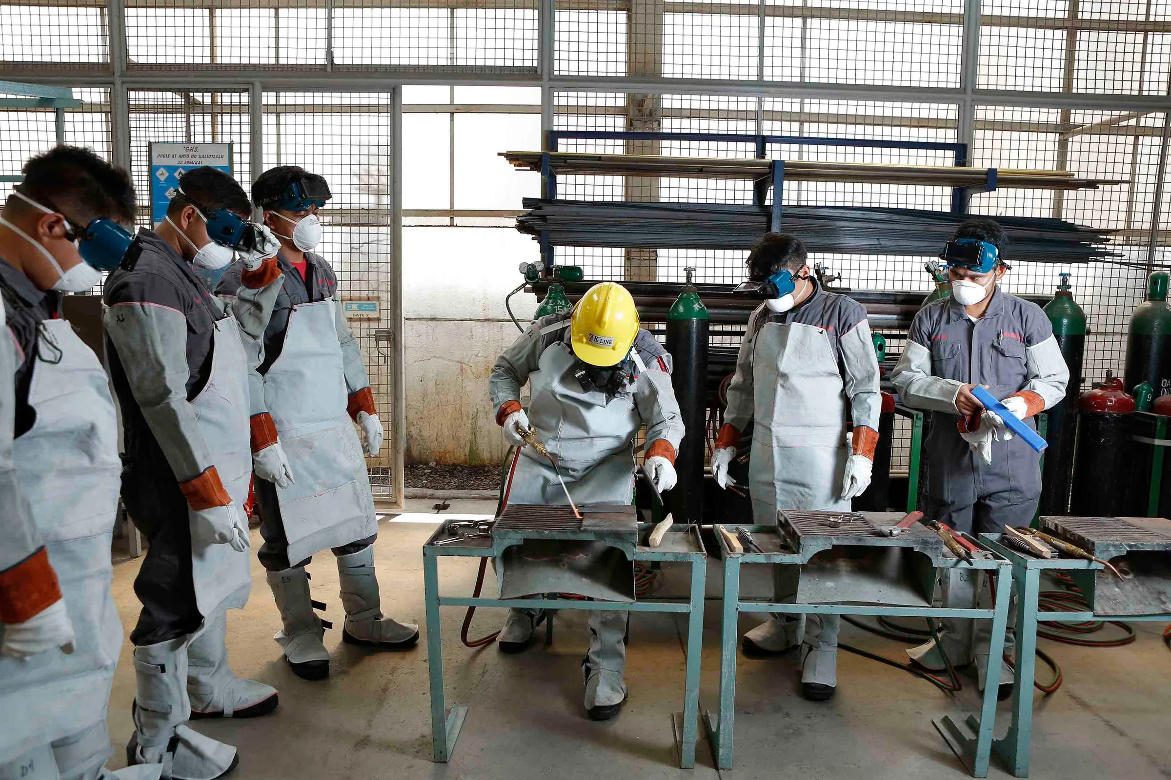 A crew in protective clothing and masks working together at a bench in a workshop